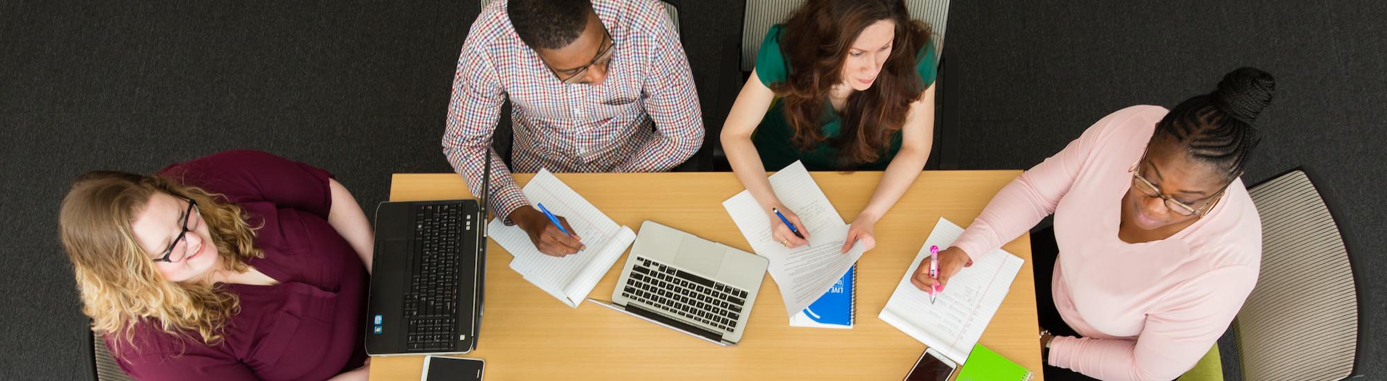 Diverse group of adults sitting around table with papers and laptops